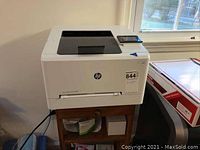 Front-right view of white HP LaserJet Pro color printer on wooden stand, with user touchscreen control panel visible.