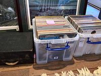 Two plastic bins filled with vinyl LP records on the floor next to framed artwork.