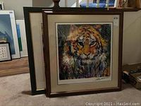 Two framed LeRoy Neiman prints leaning against wall; front is tiger portrait, behind is abstract print.