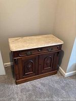 Front-left angle showing wooden base, single drawer, two cabinet doors and marble top