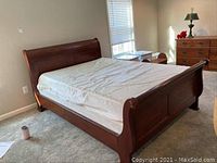 Full view of sleigh bed frame with plastic-covered mattress in bedroom.