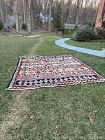 Full view of rectangular area rug laid out on grass showing overall geometric pattern and color scheme.