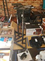 Two black adjustable On Stage Studio Speaker Stands placed on a hardwood floor among boxes and other items.