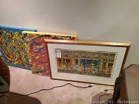 Two unframed abstract acrylic canvases leaning against wall behind a framed print