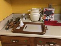 Countertop display of wooden grill tools, cutting boards, mixing bowls, bacon press, apple peeler, wooden platter