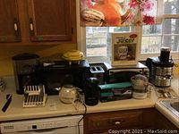 Kitchen counter with all appliances and accessories including coffee maker, microwave, juicers, toaster oven, carving knife, and disc holder.