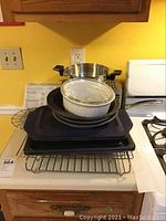 Photo of assorted kitchenware items on a stove including casseroles, cookie sheets, racks, pan, and pie pans.