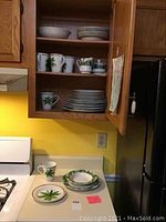 Photo showing cabinet with 8 cups featuring palm tree designs on upper shelves and stacks of plates