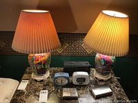 Both lamps lit on a marble-top nightstand, showing the beaded bases filled with colorful beads and beige pleated lampshades.