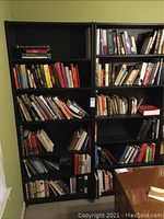 Pair of tall black particle board bookshelves filled with various books, showing wear and sagging shelves.
