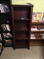 Front view of tall wooden bookcase with four shelves, stained and scratched, dark finish.