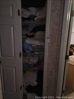 Photo of a closet with wire shelves holding several folded linens including towels, blankets, and sheets, showing some organized stacks.