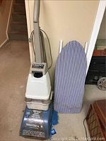 Hoover carpet shampooer and striped ironing board shown side by side on a concrete floor of a basement or lower level area.