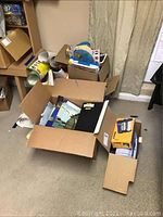 Box with various educational materials and classroom supplies including rolled posters, binders, and label maker box.