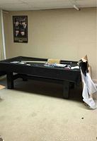 Full view of black pool table with items set on top and poster on the wall behind