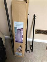 Photo of curtain rods leaning against wall beside boxed bamboo beaded curtain, showing black metal rods with pointed finials and mounting brackets.