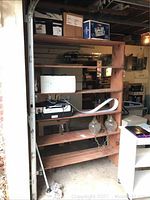 Front view of taller wooden shelving unit with multiple shelf levels, holding various items and showing overall condition in garage setting.