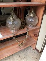 Two vintage hanging pendant lights with textured glass globes and decorative metal caps hanging on wooden shelving. Includes metal suspension chains.