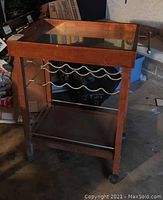 Full view of wood frame bar cart with glass top and metal wine rack beneath