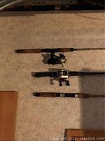 Three fishing poles laid out horizontally on garage floor, showing reel types and wood handles.
