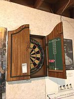 Wooden dartboard cabinet mounted on wall, doors open revealing dartboard inside