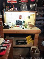 Front view of homemade wooden workbench with pegboard and objects on top and shelf below