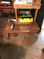 Front and angled view of wooden bench table showing shoulder cut-out and elevated small platform on one side, surface damage and paint residue, and turned wooden legs.