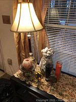 Lamp with beige fabric shade, wooden and brass base. Sitting on dark wood surface next to vase and candles.