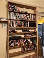 Overview of wooden shelving with multiple rows of VHS and DVD movies neatly organized, along with karaoke machine unit.