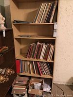 Wide view of wooden shelving containing multiple shelves filled with sheet music volumes, books, notebooks, and floppy boxes with more sheet music.