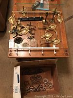 Photo of brass candle holders, hooks, towel rack, and racks laid out on table, showing wear and ornate design with floral accents