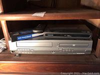 View showing the stacked Magnavox VHS player, Magnavox DVD player, black digital-analog converter box on top, remote control and VHS head cleaner tape.