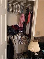 Closet wide view showing clothing on hangers including shirts and sweaters piled on a shelf, with some jackets hanging on right side