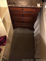 Nightstand placed between bed and shelving unit, showing front view with three drawers.