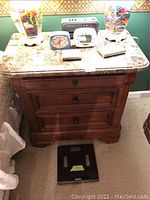 Front view of the marble top nightstand showing three drawers and two round wooden knobs per drawer. Decorative molding and curved edges visible.