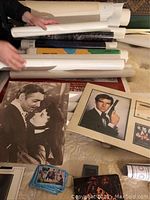 Photo of multiple rolled posters with some flat displayed, showing various movie and art posters including a black and white couple poster and a James Bond poster with Pierce Brosnan.