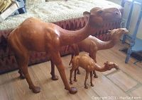 Set of three vintage molded leather dromedary camels of varying sizes shown on wooden floor with patterned bench background.
