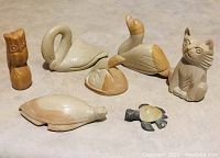 Full view of all seven stone animal carvings arranged on a light surface showing swan, duck, turtle, cat, owl, lizard and small turtle
