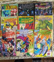 Photo showing nine Marvel Spider-Man comics including Venom, Spectacular Spider-Man, and The Amazing Spider-Man from the 1990s with worn covers and slight creases.