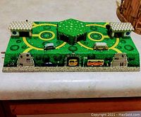 Top-down front view of vintage lithographed tin bus garage toy with checkerboard roof buildings and multiple tin buses on winding roads.