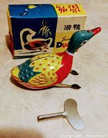 Photo of vintage lithographed tin swimming duck with winding key and original box, placed on a flat surface.