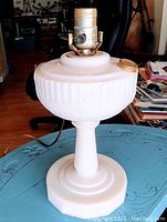 Full side view of the lamp showing its pale pink Alacite glass body, pedestal base, and electric bulb socket on top.
