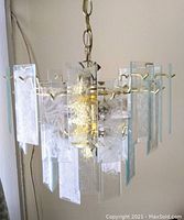 Full view of 5 light chandelier hanging on chain, showing 32 textured glass prisms with beveled edges and metal frame.