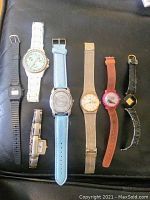 All seven watches arranged horizontally on a black surface showing different strap colors and watch face styles.
