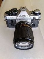 Front view of Canon AE-1 Program camera with Canon FD 135mm lens attached, showing full camera body and lens length.