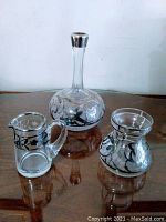 Set of 3 vintage glass pieces with silver overlay on glass: vase/decanter, creamer, and sugar bowl on reflective surface.