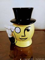 Front view of yellow ceramic Mr. Peanut jar with black top hat, monocle detail, and gloved hand on side.