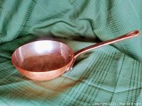 Side angled view showing copper skillet and long iron riveted handle with looped end.