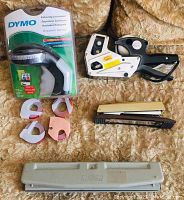 DYMO Organizer Xpress embossing label maker in sealed retail packaging with four rolls of label tape, pricing labeler, metal Rolodex 3-hole punch, Rexell stapler on fabric background