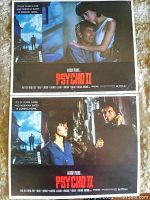 Two lobby cards from Psycho II, one showing a man and woman in close embrace, second featuring two characters, one holding a phone.